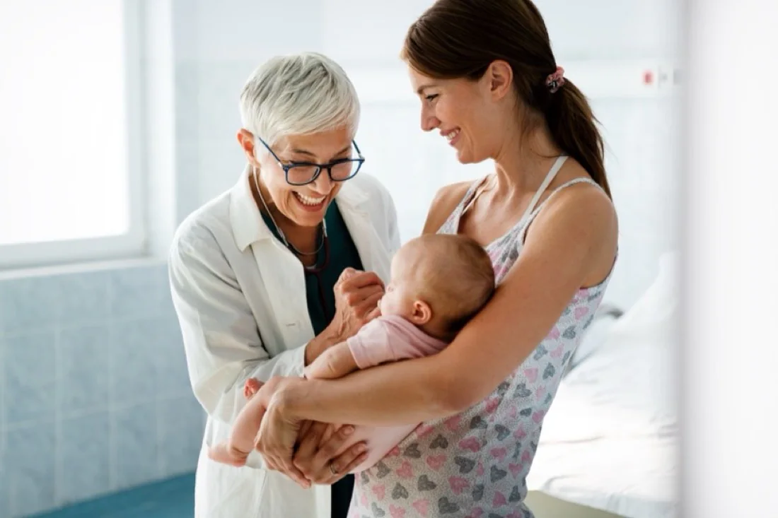 A clinician and a mother smiling over a newborn in the mother’s arms