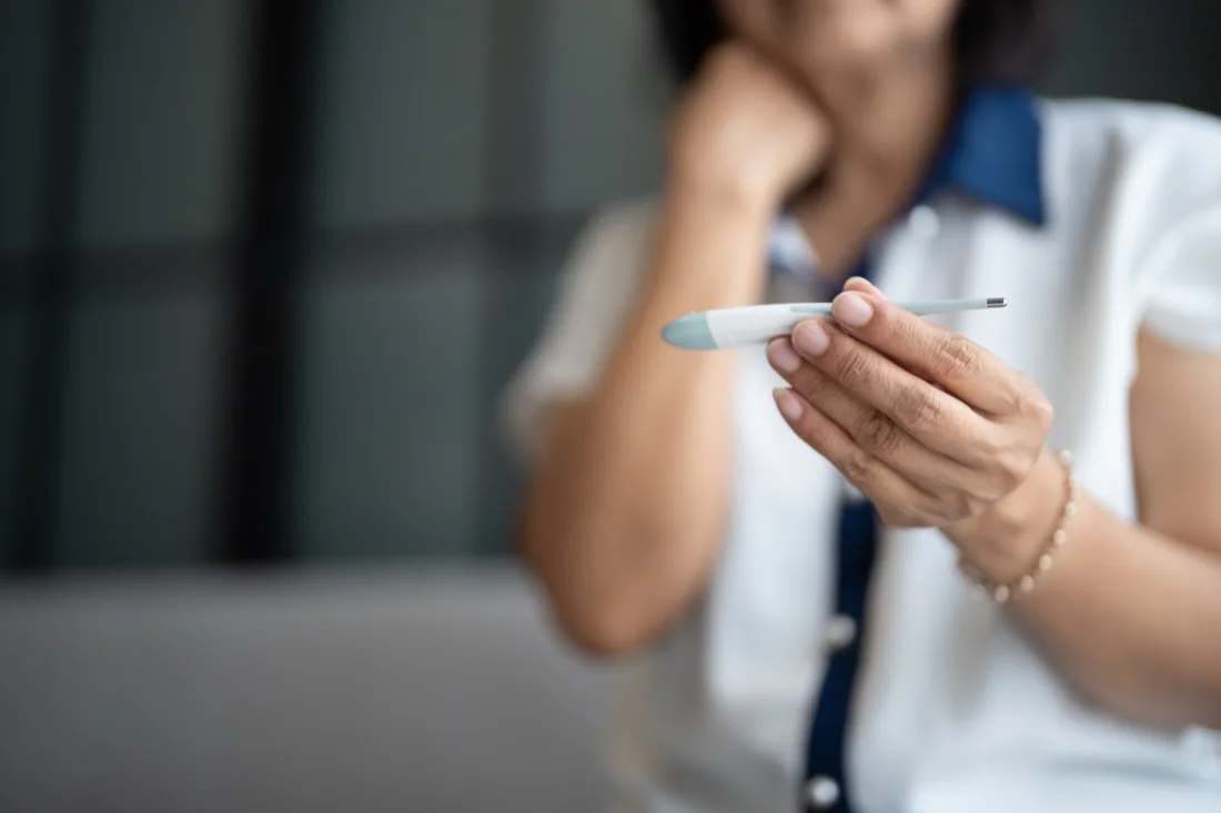 A woman checking a digital thermometer at home while feeling unwell